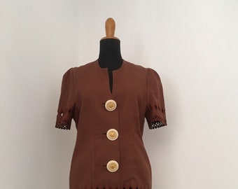 Könnte beinhalten: Eine braune Leinenjacke mit kurzen Ärmeln und einem gewellten Saum. Die Jacke hat vier goldene Knöpfe auf der Vorderseite.