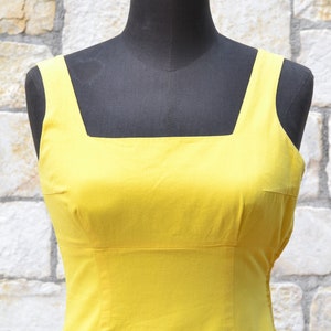 May include: A sleeveless yellow dress with a square neckline. The dress is made of a smooth, lightweight fabric.