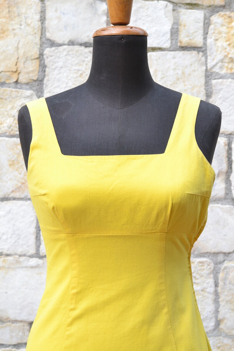 May include: A sleeveless yellow dress with a square neckline. The dress is made of a smooth, lightweight fabric.