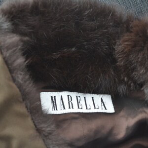 K&ouml;nnte beinhalten: Ein brauner Pelzkragen mit einem wei&szlig;en Etikett, auf dem "MARELLA" steht, an einer braunen Jacke.