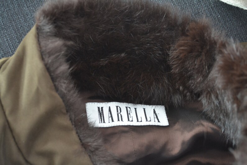K&ouml;nnte beinhalten: Ein brauner Pelzkragen mit einem wei&szlig;en Etikett, auf dem "MARELLA" steht, an einer braunen Jacke.