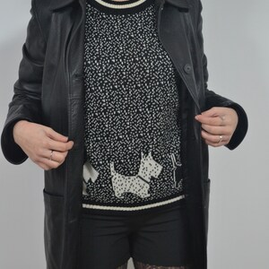 May include: A black leather jacket with a black and white patterned sweater featuring a white dog design. The person is wearing black shorts and black patterned tights.