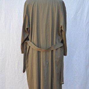 May include: A long, khaki-colored trench coat with a belt. The coat is hanging on a mannequin.
