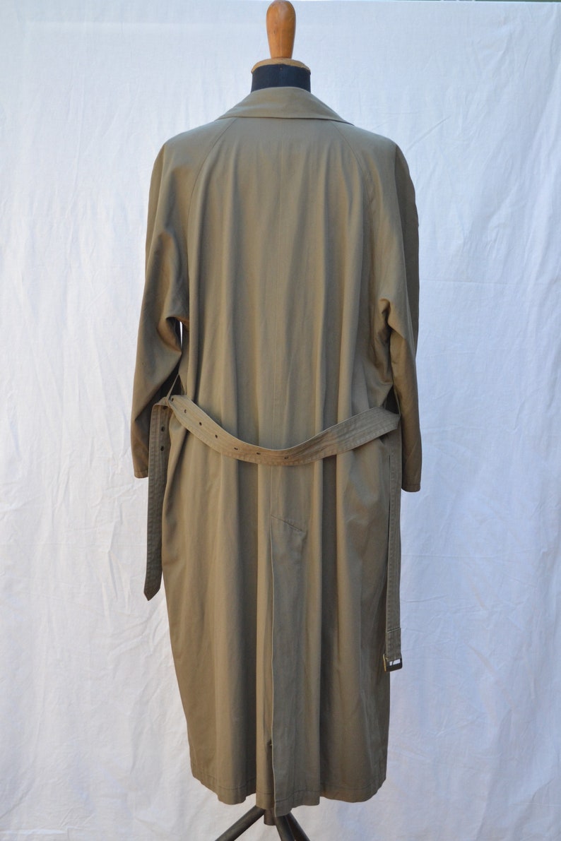 May include: A long, khaki-colored trench coat with a belt. The coat is hanging on a mannequin.