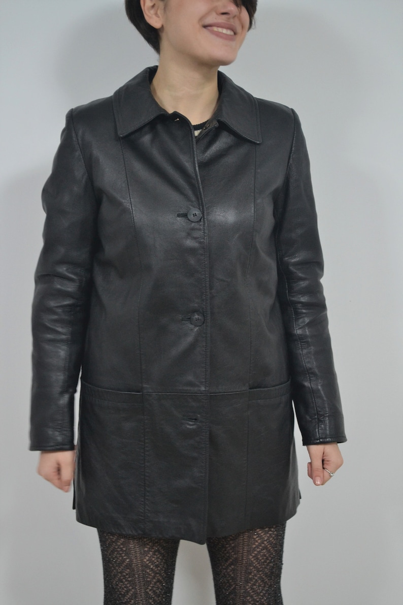 May include: A black leather jacket with a collar, long sleeves, and a button-up front. The jacket has two pockets on the front and a single pocket on the left chest.