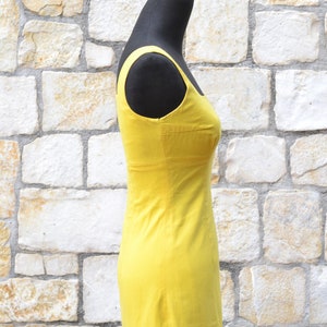 May include: A bright yellow sleeveless dress on a mannequin. The dress has a simple, fitted silhouette and a straight neckline.