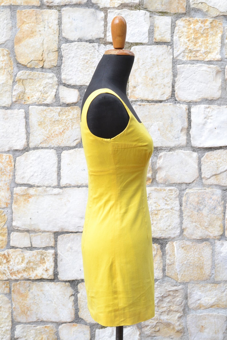 May include: A bright yellow sleeveless dress on a mannequin. The dress has a simple, fitted silhouette and a straight neckline.