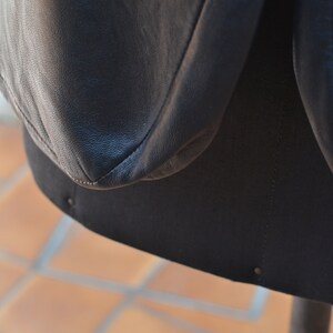 May include: Close-up of a black leather jacket with a seam detail. The jacket is on a mannequin and the background is a tiled floor.