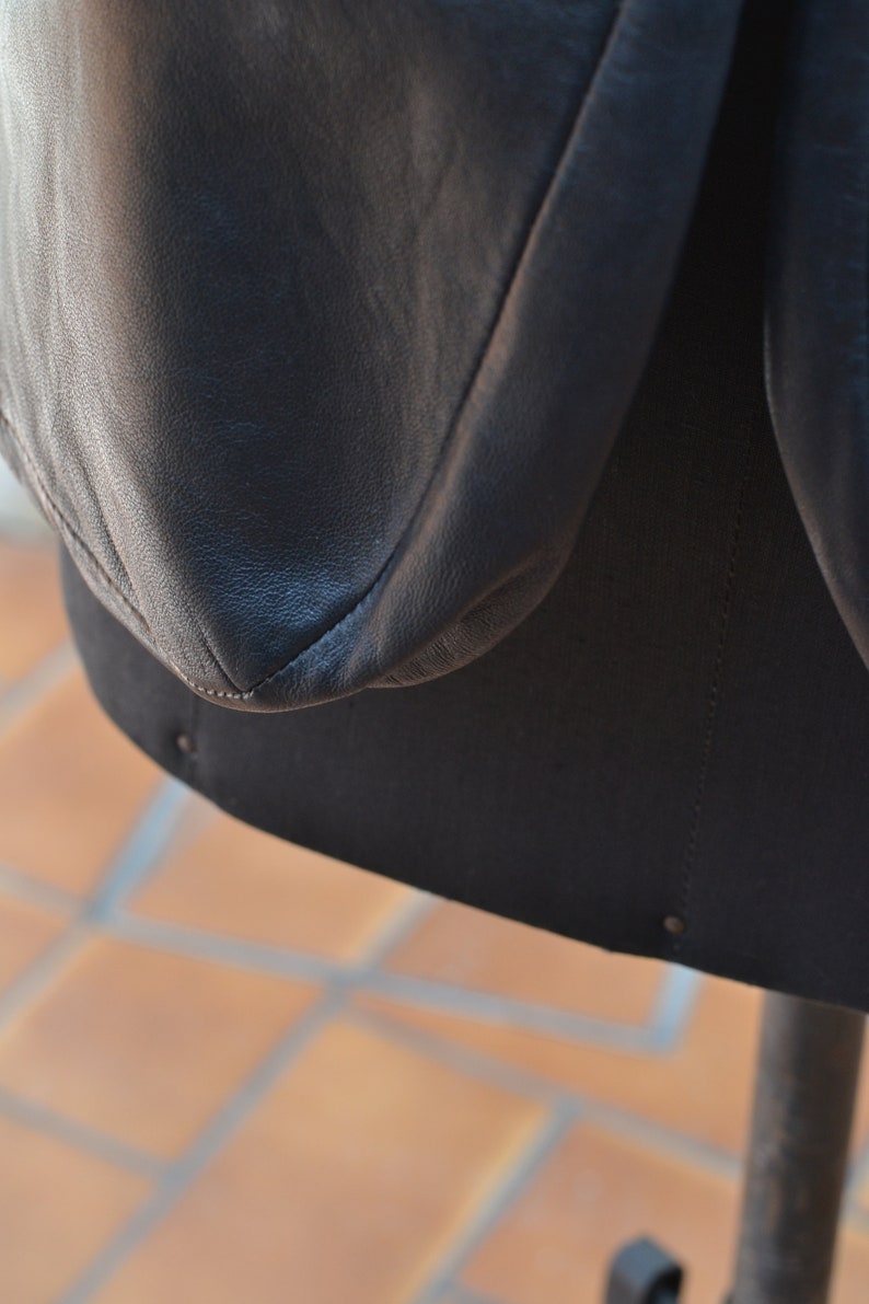 May include: Close-up of a black leather jacket with a seam detail. The jacket is on a mannequin and the background is a tiled floor.