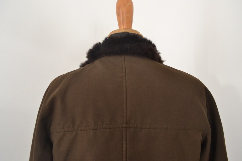 K&ouml;nnte beinhalten: Eine braune Jacke mit einem schwarzen Pelzkragen. Die Jacke hat einen Rei&szlig;verschluss und eine Naht auf der R&uuml;ckseite.