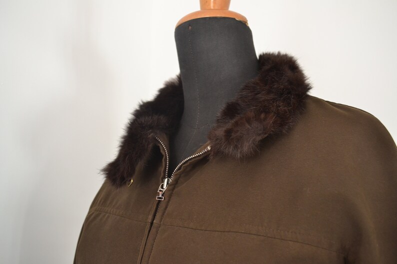 K&ouml;nnte beinhalten: Eine braune Jacke mit einem Pelzkragen. Die Jacke hat einen Rei&szlig;verschluss und ein braunes Futter.