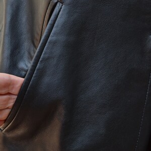 May include: Close-up of a black leather jacket with a pocket. The leather has a textured surface.