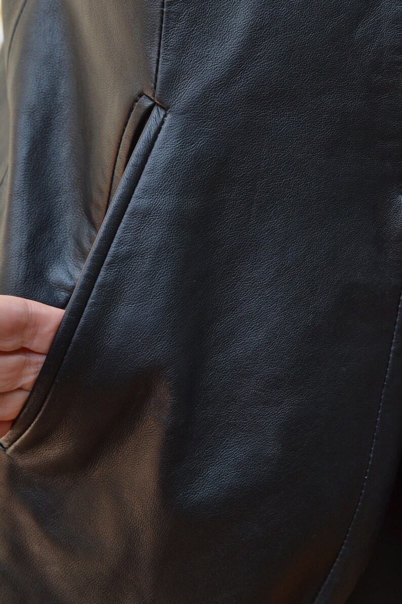 May include: Close-up of a black leather jacket with a pocket. The leather has a textured surface.