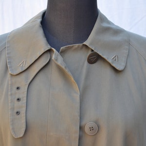 May include: A green, long-sleeved jacket with a collar and two buttons. The jacket has a small logo on the collar and a larger logo on the button.