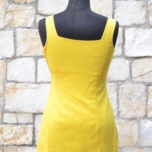 May include: A sleeveless yellow dress with a square neckline. The dress is fitted and has a straight skirt.