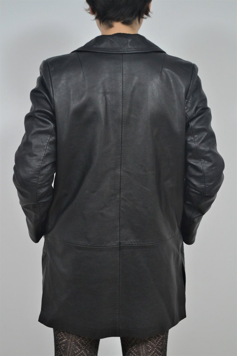 May include: A black leather jacket with a long, fitted style. The jacket has a classic collar and a single-breasted closure.