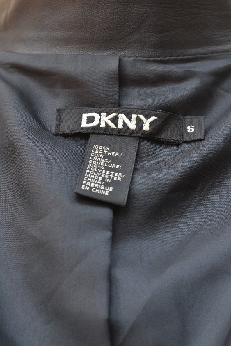 May include: A black leather jacket with a DKNY label and a size 6 tag. The label lists the material as 100% leather and the lining as 100% polyester. The jacket was made in China.