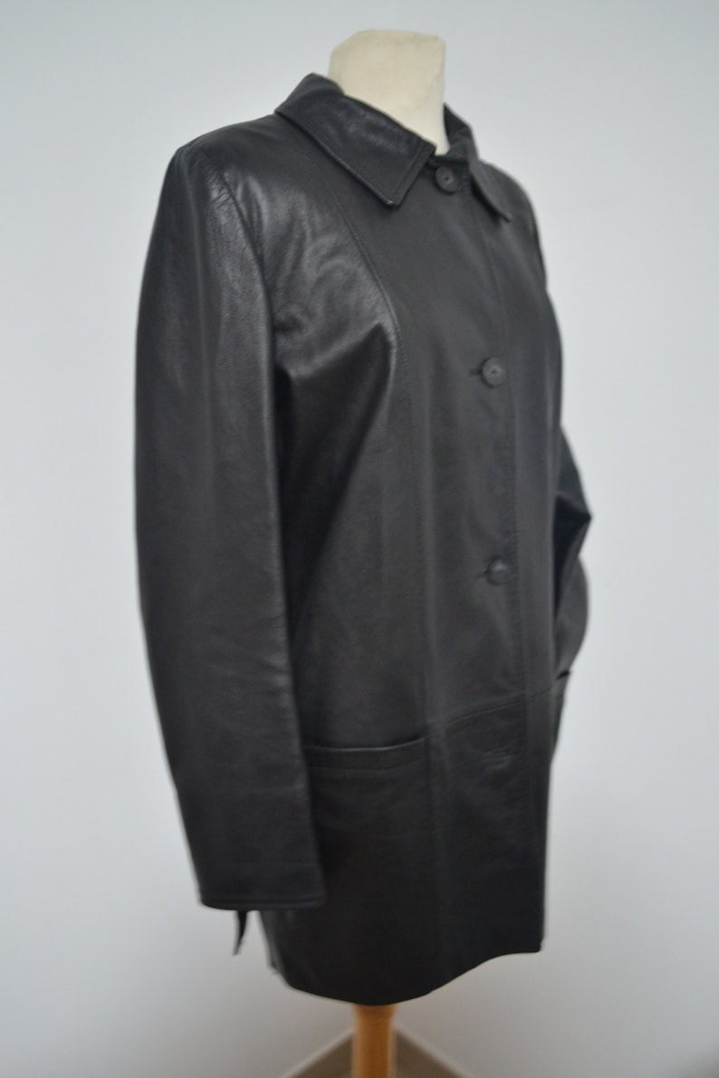 May include: A black leather coat with a collar and button closure. The coat has a long, straight silhouette and two pockets.
