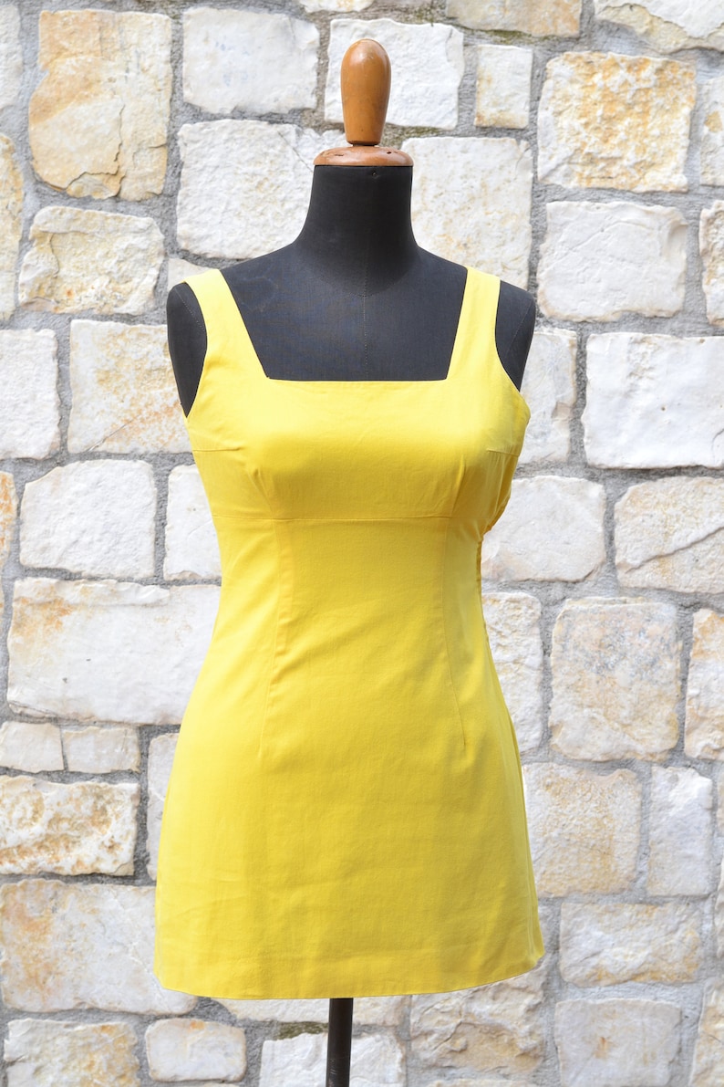 May include: A sleeveless yellow dress with a square neckline and a fitted silhouette.