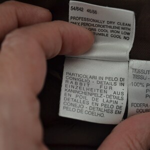 K&ouml;nnte beinhalten: Nahaufnahme eines braunen Stofflabels mit wei&szlig;em Text. Der Text lautet "Professionally dry clean only, perchloroethylene with colors cool iron low, tumble cool no." Das Etikett enth&auml;lt auch Details zur Stoffzusammensetzung, darunter "100% poliestere, polyester, poliester" und "Fodera-lining-futter, doublure, forro".