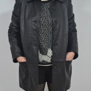 May include: A black leather jacket with a button closure and pockets. The jacket is worn over a white and black patterned sweater.