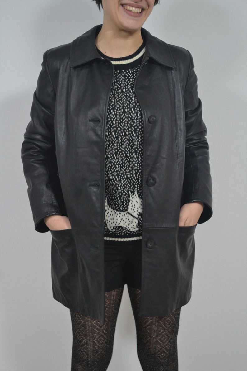 May include: A black leather jacket with a button closure and pockets. The jacket is worn over a white and black patterned sweater.