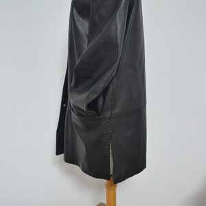 May include: A black leather jacket with a collar and a zipper closure. The jacket has a long, straight cut and a single pocket on the left side.