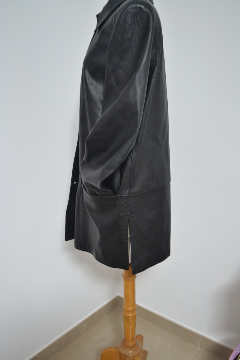 May include: A black leather jacket with a collar and a zipper closure. The jacket has a long, straight cut and a single pocket on the left side.