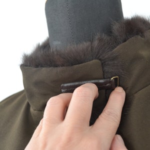 K&ouml;nnte beinhalten: Eine braune Jacke mit einem Pelzkragen und einem braunen Lederriemen mit einer Metallschnalle.
