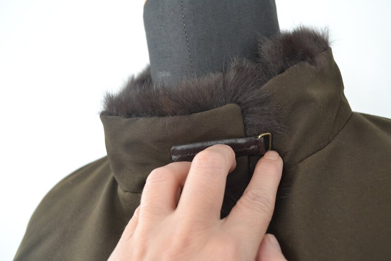 K&ouml;nnte beinhalten: Eine braune Jacke mit einem Pelzkragen und einem braunen Lederriemen mit einer Metallschnalle.