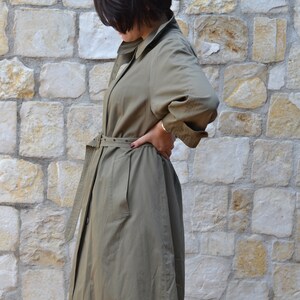 May include: A khaki trench coat with a belt and a button closure. The coat has a long sleeve and a relaxed fit.