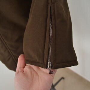 K&ouml;nnte beinhalten: Nahaufnahme einer braunen Jacke mit einem Rei&szlig;verschlussdetail am &Auml;rmel.
