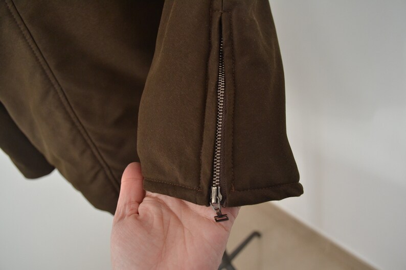 K&ouml;nnte beinhalten: Nahaufnahme einer braunen Jacke mit einem Rei&szlig;verschlussdetail am &Auml;rmel.