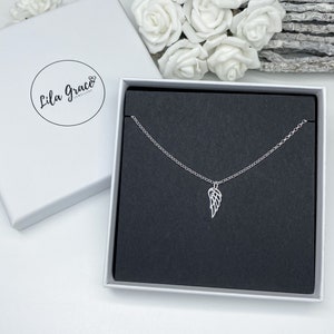 May include: A silver necklace with a delicate angel wing pendant, displayed in a black jewellery box with a white lid. The box has the text "Lila Grace Jewellery" printed on the lid.
