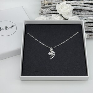 May include: A silver necklace with a delicate chain and a small angel wing charm with a clear crystal. The necklace is displayed in a black velvet box.