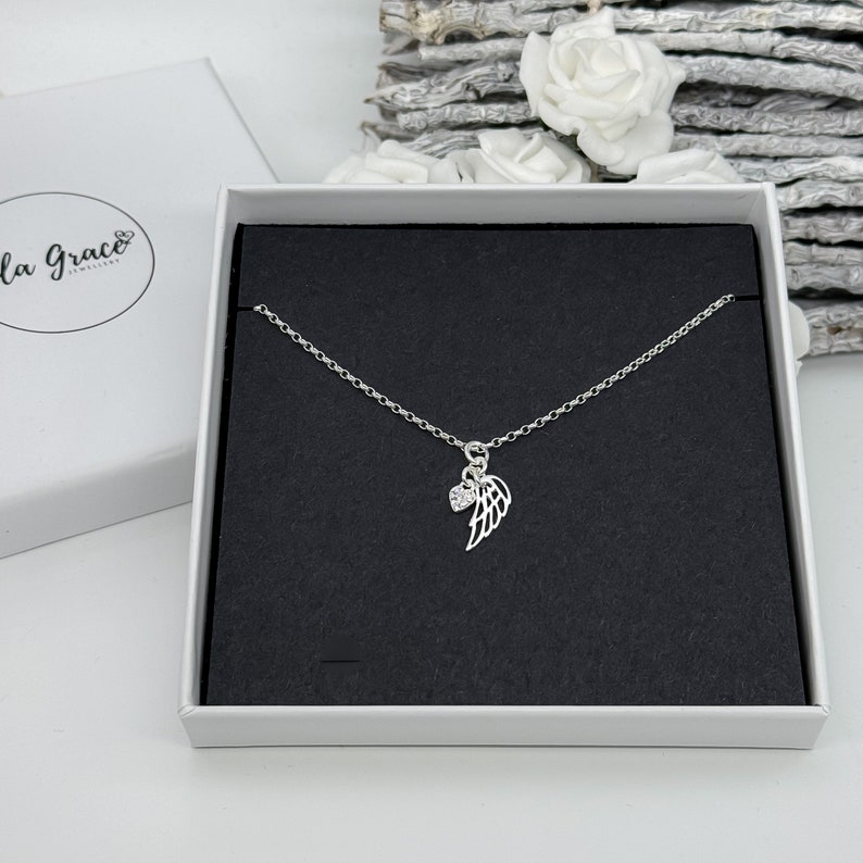 May include: A silver necklace with a delicate chain and a small angel wing charm with a clear crystal. The necklace is displayed in a black velvet box.