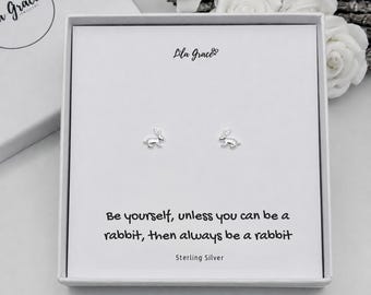 May include: A pair of silver rabbit stud earrings presented in a white gift box. The card features the text 'Lila Grace', 'Sterling Silver', and 'Be yourself, unless you can be a rabbit, then always be a rabbit'. The earrings are small and metallic.