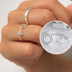Peut inclure: Bague en argent avec un motif d'abeille et d'hexagone. La bague est réglable et peut être portée à n'importe quel doigt.