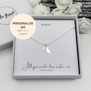 Könnte beinhalten: Halskette aus Sterlingsilber mit Katzenanhänger und Initialenbuchstaben, präsentiert in einer Geschenkbox. Auf der Karte steht "All you need is love and a cat". Die Halskette kann mit 1 oder 2 Buchstaben personalisiert werden.