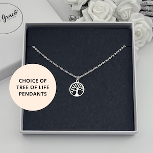 May include: A silver-toned necklace featuring a circular tree of life pendant on a delicate chain, presented in a square black-lined gift box. A circular overlay on the left side displays the text: CHOICE OF TREE OF LIFE PENDANTS.