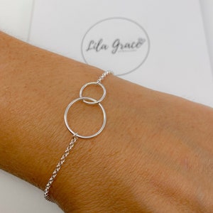 May include: A silver chain bracelet with two interlocking circles. The bracelet is on a person's wrist.