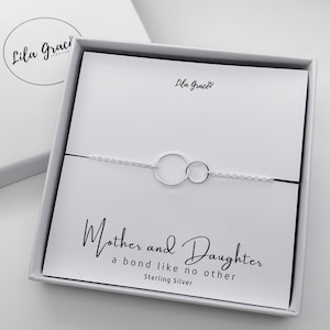 Peut inclure: Un bracelet en argent avec deux cercles entrelacés, présenté dans une boîte blanche avec le texte "Mère et Fille un lien comme aucun autre Argent Sterling".