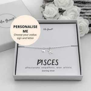 May include: A silver bracelet with a heart charm and a Pisces symbol, displayed in a white gift box. The box features the text "PISCES" and the words "affectionate. empathetic. wise. artistic. Sterling Silver."