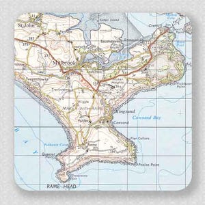 May include: Square coaster with a detailed map of the Maker-with-Rame area, including Millbrook, Kingsand, and Rame Head. The map shows roads, place names, and elevation markings. The color scheme is beige, blue, and brown, with a grid overlay.