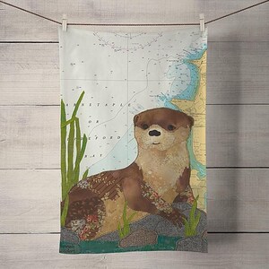 May include: A brown and tan otter with a patchwork design is sitting on a rock with green reeds in the background. The otter is on a nautical chart with the text "Barnstaple" and "Lyefford Bay".
