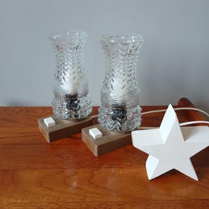 Könnte beinhalten: Zwei Vintage-Tischlampen aus Glas mit strukturierten Glasschirmen und braunen Sockeln mit weißen Kippschaltern. Die Lampen stehen auf einer Holzoberfläche mit einem weißen sternförmigen Objekt.