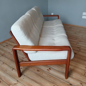 Könnte beinhalten: Ein weißes Stoff-Sofa mit einem Gestell aus Teakholz. Das Sofa hat ein gestepptes Design und steht auf einem Holzboden.