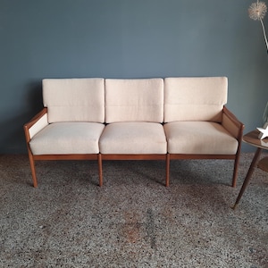 Könnte beinhalten: Ein dreisitziges Sofa mit einer hellbeigen Stoffpolsterung und einem dunklen Holzrahmen. Das Sofa hat ein schlichtes Design mit einer niedrigen Rückenlehne und Armlehnen.