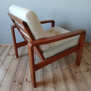 Könnte beinhalten: Ein moderner Sessel aus der Mitte des Jahrhunderts mit einer hellbeigen Stoffpolsterung und einem dunklen Holzrahmen. Der Sessel hat eine niedrige Rückenlehne und eine breite Sitzfläche. Der Sessel steht auf einem Holzboden.