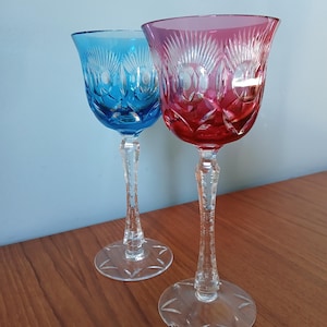 Könnte beinhalten: Zwei hohe, klare Weingläser aus Glas mit aufwendigen Schnitzereien. Ein Glas ist blau und das andere rosa.